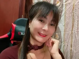 Aly_live poses with a smile, wearing a dark red top and showing her long dark hair in an indoor setting.