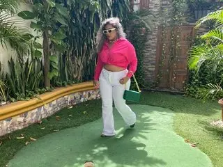 Stylish woman in a bright pink crop top and white trousers posing in a lush tropical garden setting.