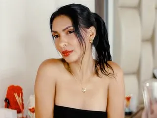 Alysonaa looks at the camera with red lipstick and dark hair pulled back in a ponytail while wearing a black tube top.