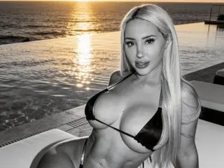 AmandaAndrews poses in a black bikini top while relaxing by a pool at sunset, showing off her long blonde hair and cleavage.