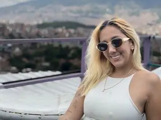 Amanda_klaire smiles while wearing sunglasses and a white tank top, posing outdoors with her long blonde hair down.