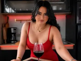 Smiling woman in a red tank top enjoying red wine in a modern kitchen with warm ambient lighting.