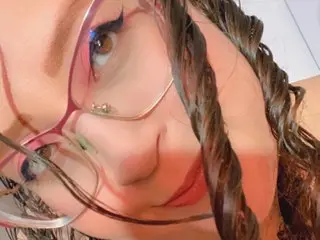 Amberbedoya_18 looks into the camera with her dark hair in long, tight curls and wears thin-rimmed glasses.