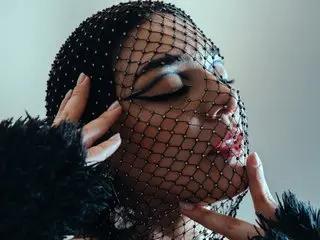 Elegant woman in vintage black beaded veil and faux fur outfit posing with a moody, glamorous aesthetic.