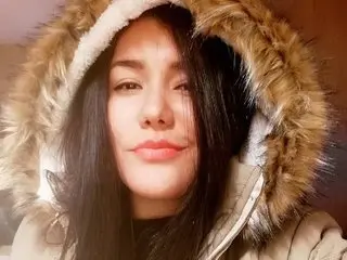 AmmyHil shows her face and long dark hair while wearing a light-colored hooded jacket with thick, fluffy fur trim.
