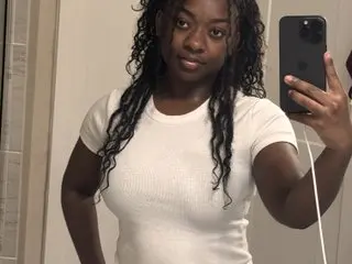 Amourmywayy poses in a white t-shirt, showing her long, curly dark hair and natural skin in a mirror selfie.