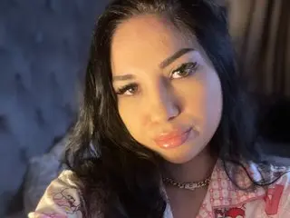 Young woman with long dark hair wearing pink patterned pajamas in a dimly lit room.