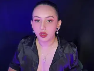 Glamorous woman in a black satin shirt and bold red makeup posing against a moody blue background.