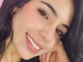 AnaSofiaFoxx smiles while resting her chin on her hands, showing her long dark hair and clear skin.