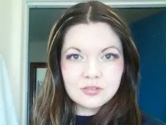 Angel22222 poses for a close-up headshot, showing her long brown hair and light makeup against a plain indoor background.