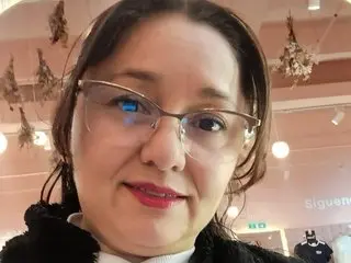 AngelRouss looks directly at the camera wearing clear-framed glasses and a black top, with her dark hair pulled back.