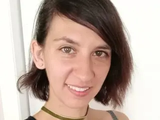 Smiling woman with short dark hair wearing a gold choker necklace in a bright indoor setting.