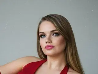Angelina88888 poses with her long brown hair down, wearing a red top against a plain grey background.