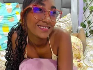 Angelina_Murphy smiles while wearing a white camisole, showing her long dark curly hair and bare shoulders in a bright room.
