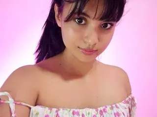 AngellaDevi poses in a floral off-the-shoulder top against a pink background.