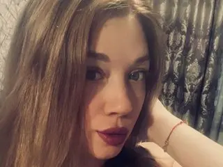 Close-up portrait of a woman with long brown hair and dark lipstick posing in a cozy indoor setting.