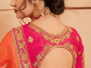Anjalindin999 poses with her dark hair in a bun, wearing a bright pink embroidered blouse and a matching orange sari.