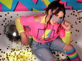 Smiling woman in retro pink graphic tee and neon accessories sitting by a disco ball in a 90s party setting.