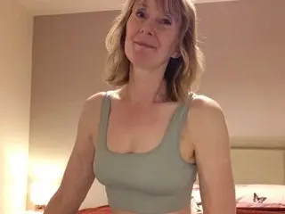 Smiling blonde woman in a sage green crop top relaxing in a cozy bedroom setting.
