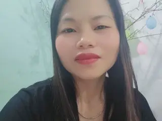 AnnaSexyy poses with long dark hair and red lipstick, wearing a black top against a light green background.