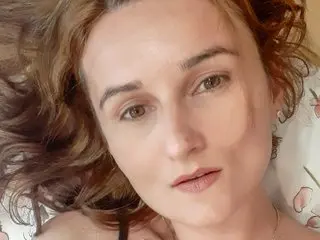 AnneRos looks directly at the camera with her wavy brown hair framing her face in a close-up headshot.