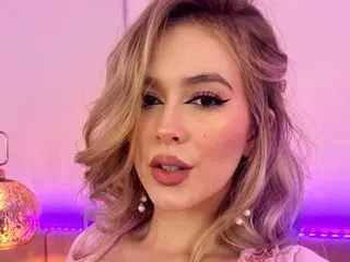 Blonde woman with winged eyeliner and pink makeup posing in soft purple ambient lighting.