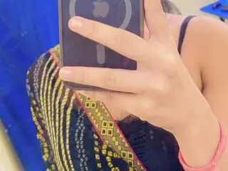 AnnuDarlingInd poses for a mirror selfie, wearing a black and gold patterned top with thin straps, holding her phone up to her face.