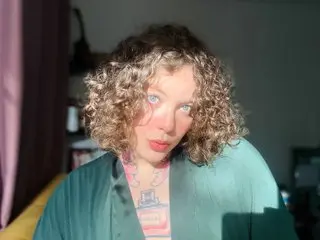 Curly-haired woman in a green silk robe relaxing in soft sunlight.