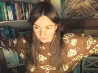 AntoniaPur28 has long brown hair and is wearing a brown patterned long-sleeve top while looking down.