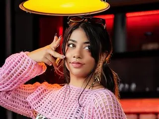 AnyaFord poses with a hand near her face, wearing a pink mesh top with her dark hair styled down.