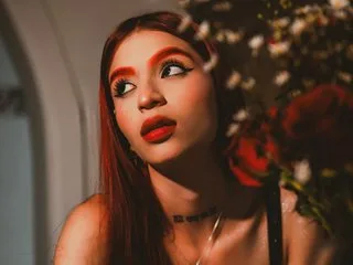 Apriiljonnes — Apriiljonnes with long red hair and bold makeup poses near a bouquet of flowers.