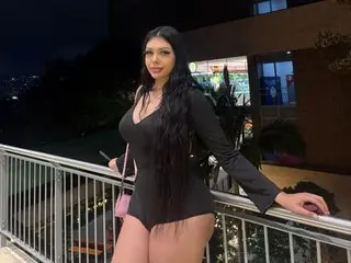 April77 poses outdoors at night wearing a tight black long-sleeve bodysuit that shows off her curves and long dark hair.