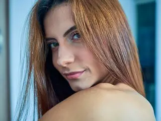 AprilJakovish looks over her shoulder with long brown hair, showing her bare shoulder and neck in a close-up shot.