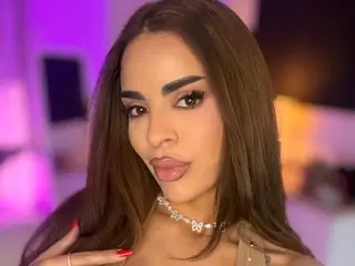 Arabian_Rose poses close-up, showing her face, long brown hair, and a silver necklace while wearing a light-colored top.