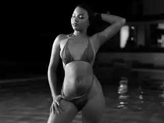 AriadnaLoreen poses in a black and white photo wearing a tiny triangle bikini, showing off her bare stomach and hips against a dark background.
