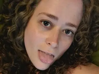 ArieLabai licks her lips while looking at the camera with her curly hair framing her face.