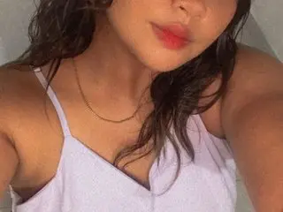 Arielasm poses close up, showing her face, dark wavy hair, and white camisole top.