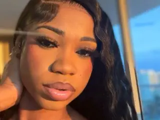 Artistworldd poses close-up, showing her face, dark wavy hair, and soft lips against a bright, soft-focus background.