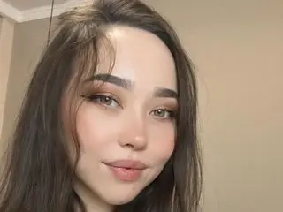 As1anGirlfriend looks directly at the camera with long dark hair and soft makeup, showing her face and shoulders against a plain background.