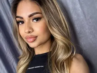 Asha_Yuvas poses close-up, looking at the camera with her long blonde-highlighted hair framing her face.