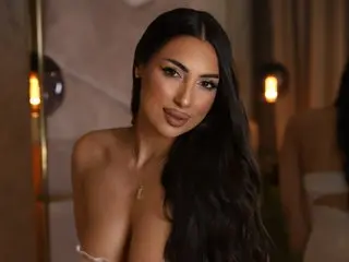 AshleyNoir poses with long, wavy black hair, wearing a low-cut top that shows off her cleavage and chest.