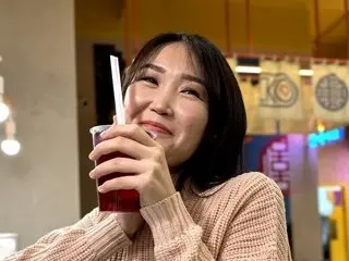AsianVelvet smiles while sipping a red drink through a straw in a cozy indoor setting.