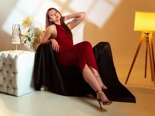 AudreyQuinn poses in a red dress, leaning back against a black chair with her hands resting on her legs and a soft smile.