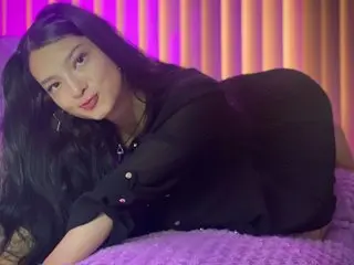 AuroraPalmerr with long dark hair poses in a black dress while laying on a purple bed.
