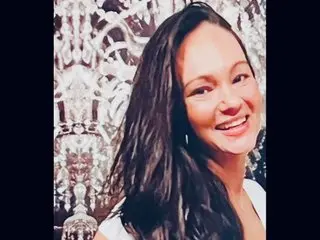 Smiling brunette woman in a white top posing against an elegant silver patterned backdrop.
