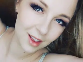 AussieCosplay looks at the camera with a soft smile, showing her face and light blonde hair against a plain background.