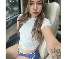 Autumn2704 poses in a white tank top, showing her long wavy hair and light skin while sitting in a white car seat.