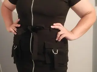 AvaRose_XXX poses in a black sleeveless zip-up top and matching cargo shorts, showing off her curves against a plain white wall.