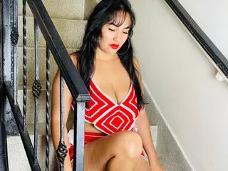 AzumiWalker poses on a staircase wearing a red and white striped bikini, showing her cleavage and long dark hair.