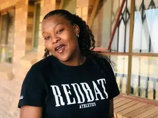 BLCKCANDY90 wearing a black REDBAT athletics t-shirt, looking at the camera with her hair in long braids while sitting outdoors.